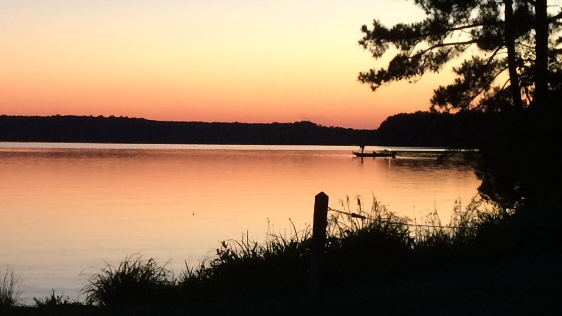 Calm lake at sunrise with a solitary boat silhouette against orange sky